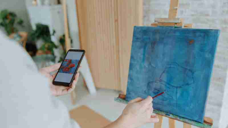 Artist uses smartphone to guide painting process on canvas indoors., tags: debat - pexel