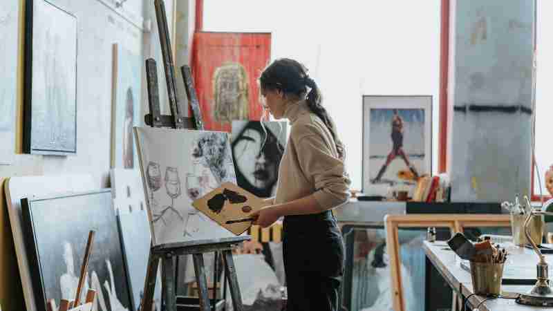 A woman artist works on a painting in a creative studio space filled with art and light., tags: en - pexel